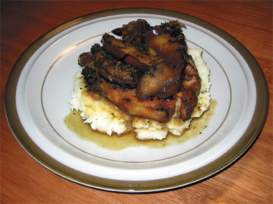 Pork chops sit on a pile of mashed potatoes, topped with Red Delicious apples and a pan sauce. 