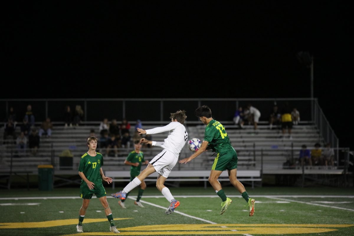 Oakville midfielder Tyler Maddock (3) and Lindbergh backfield Arnes Dakic (13) jump in unison, each attempting to head the ball and take possession. Lindbergh players Grant Evans (17) and Kenan Jakupovic (5) tensely watch from the background.