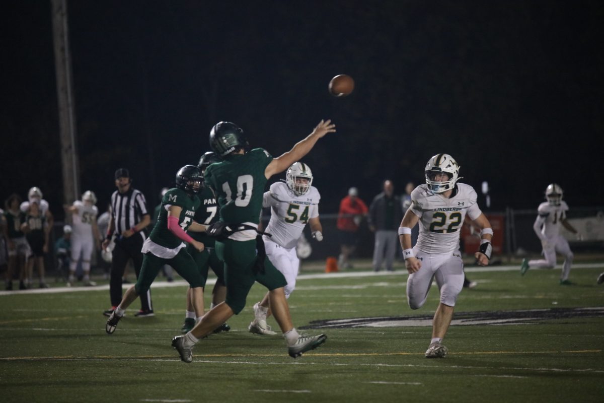 Mehlville quarterback Dan Grimm (10), pictured above, passes downfield as Lindbergh linebacker Brody Wharton (22) approaches for the tackle. Lindbergh and Mehlville players follow, running downfield.