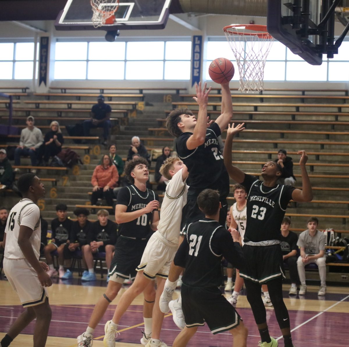 Mehlville player Allen Kujundzic (25) goes for the layup surrounded by teammates and opponents as they all reach and watch.
