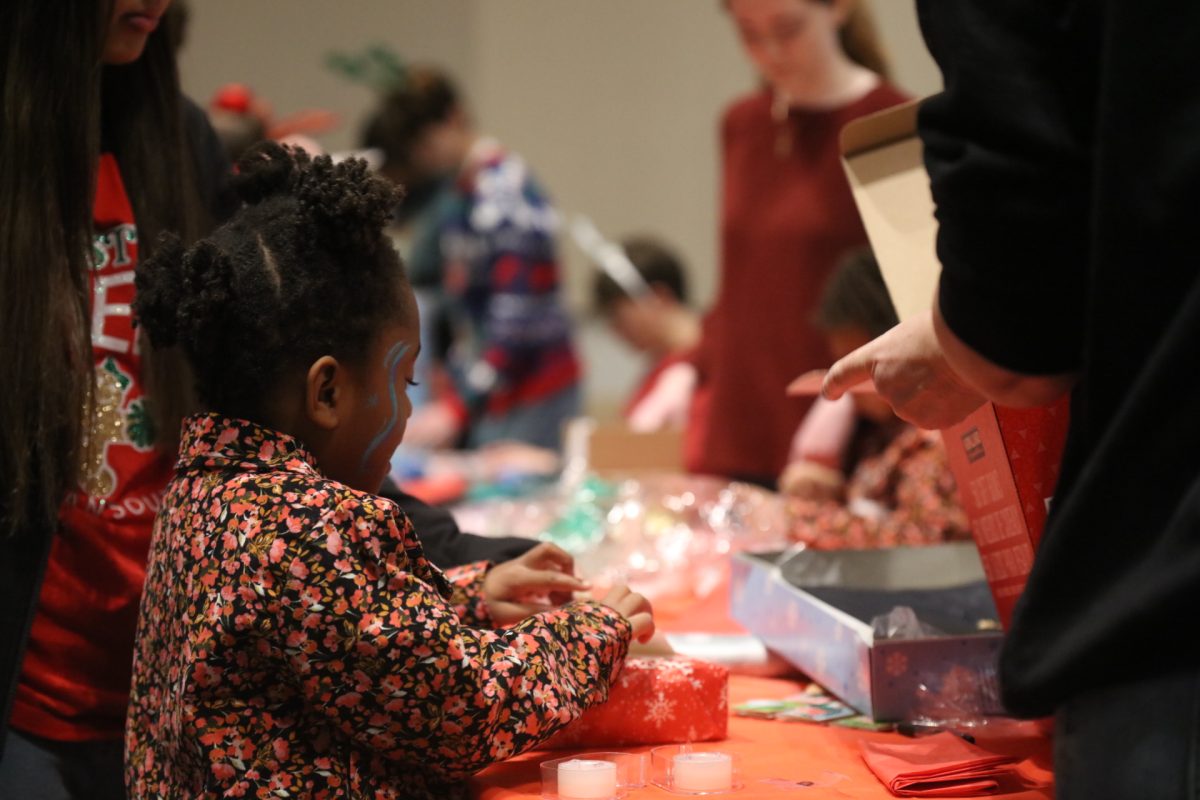 A young girl with face paint wraps her present to give to her foster parent. 