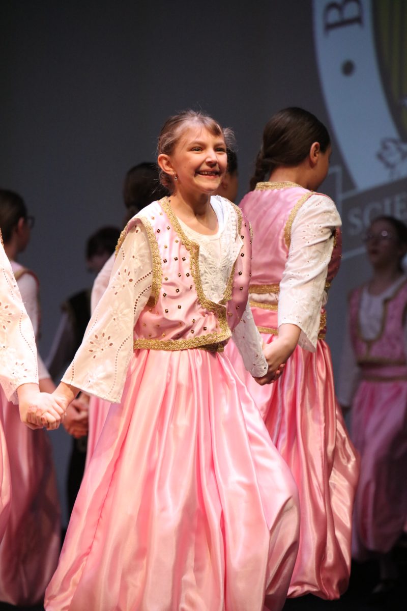 A performer jumps and smiles, linked in a circle with others on stage.