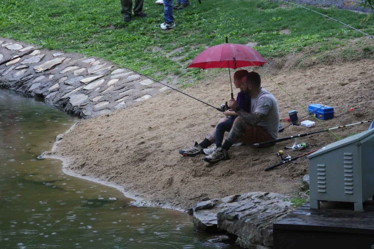 A father and son sit on the sand sharing an umbrella.