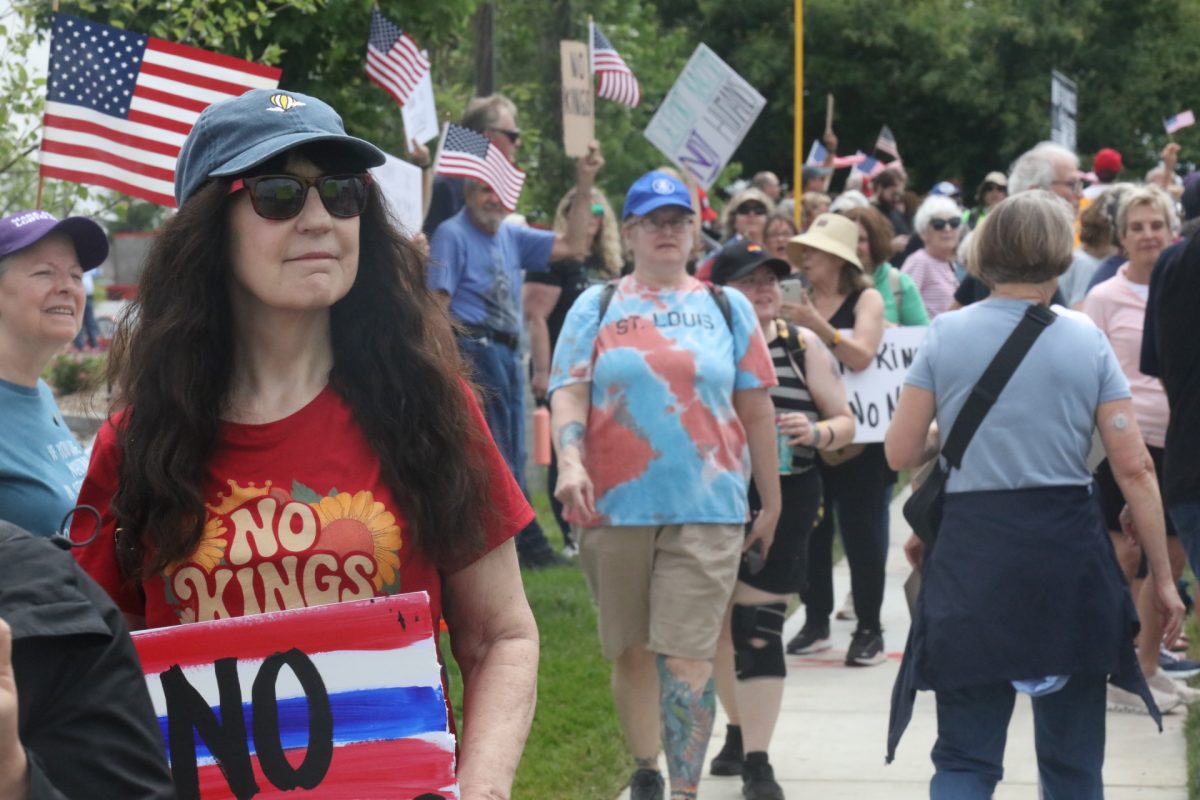 A woman wearing a shirt reading "No Kings" holds a sign with the same message.