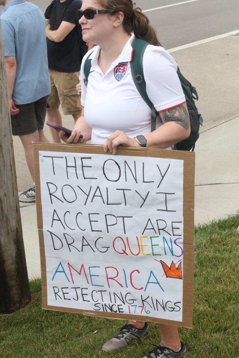 A protestor holds a sign reading "The only royalty I accept are drag queens. America rejecting kings since 1776." 