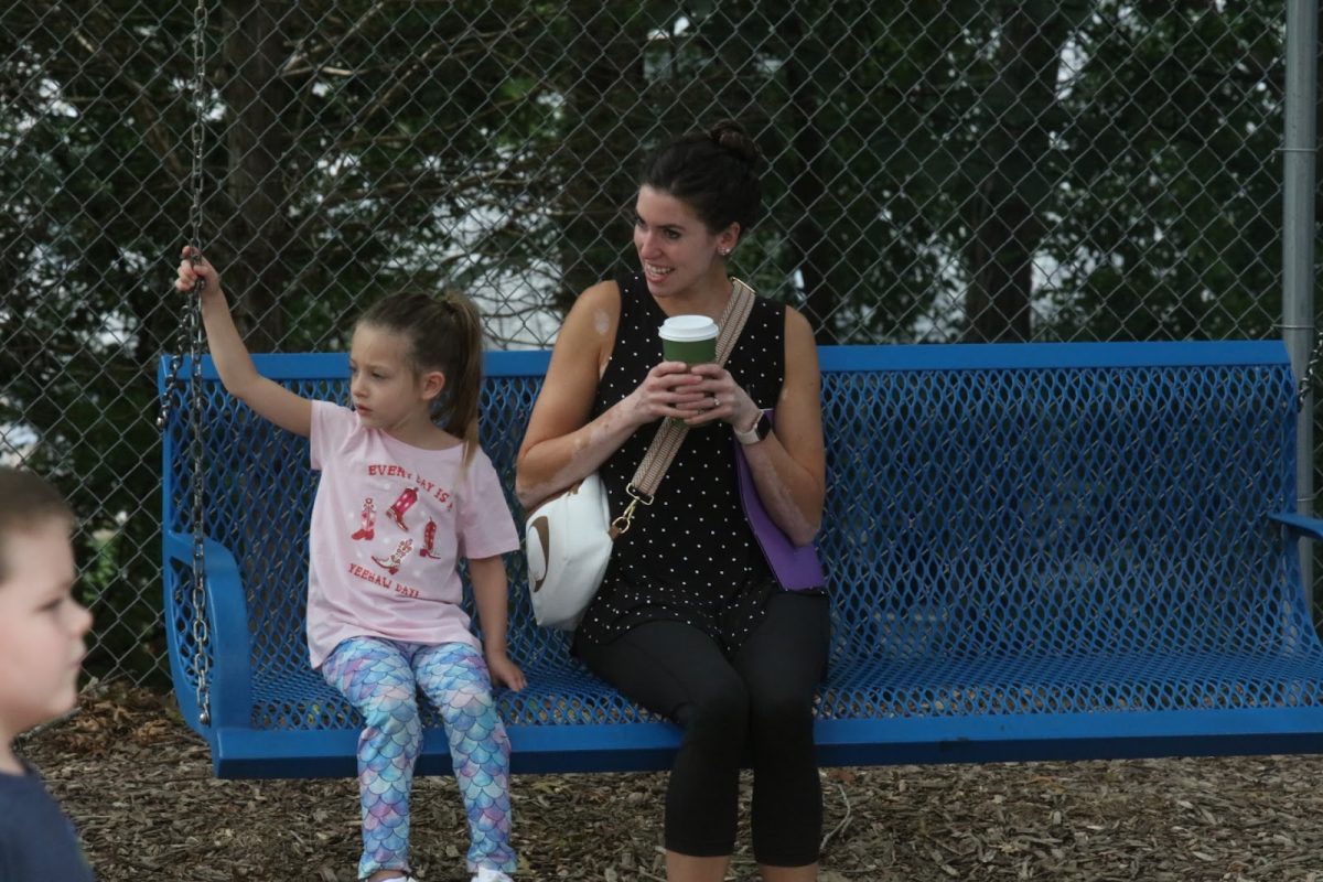 A parent sits with her child on the swinging bench.