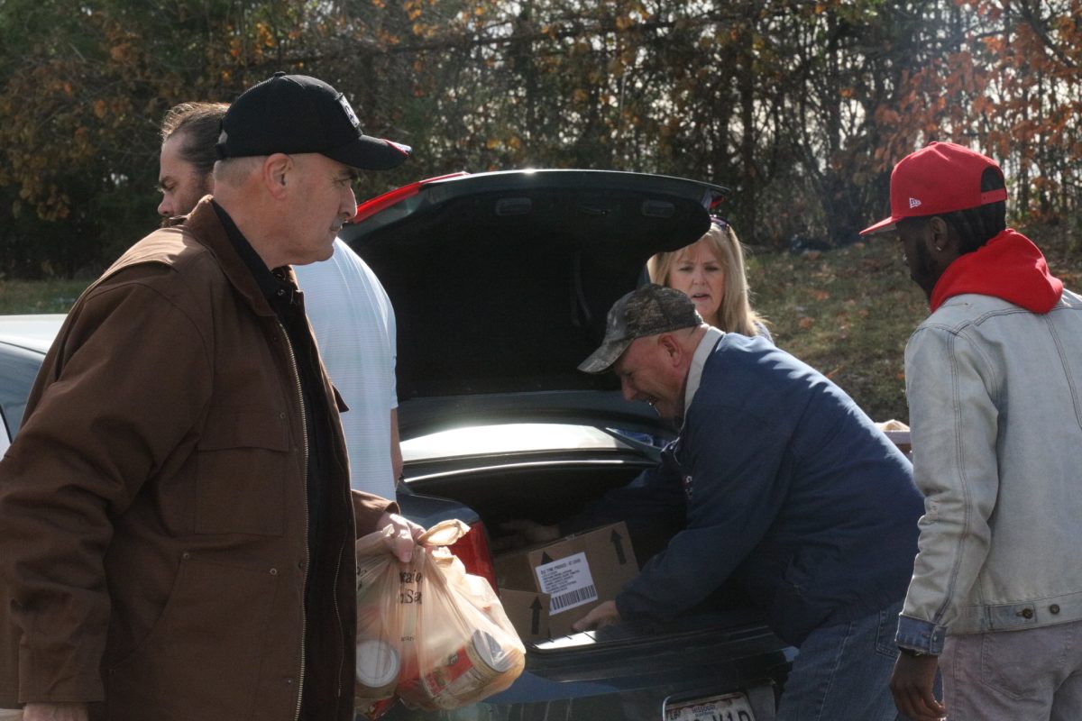 Volunteers load food items into an attendee's car.