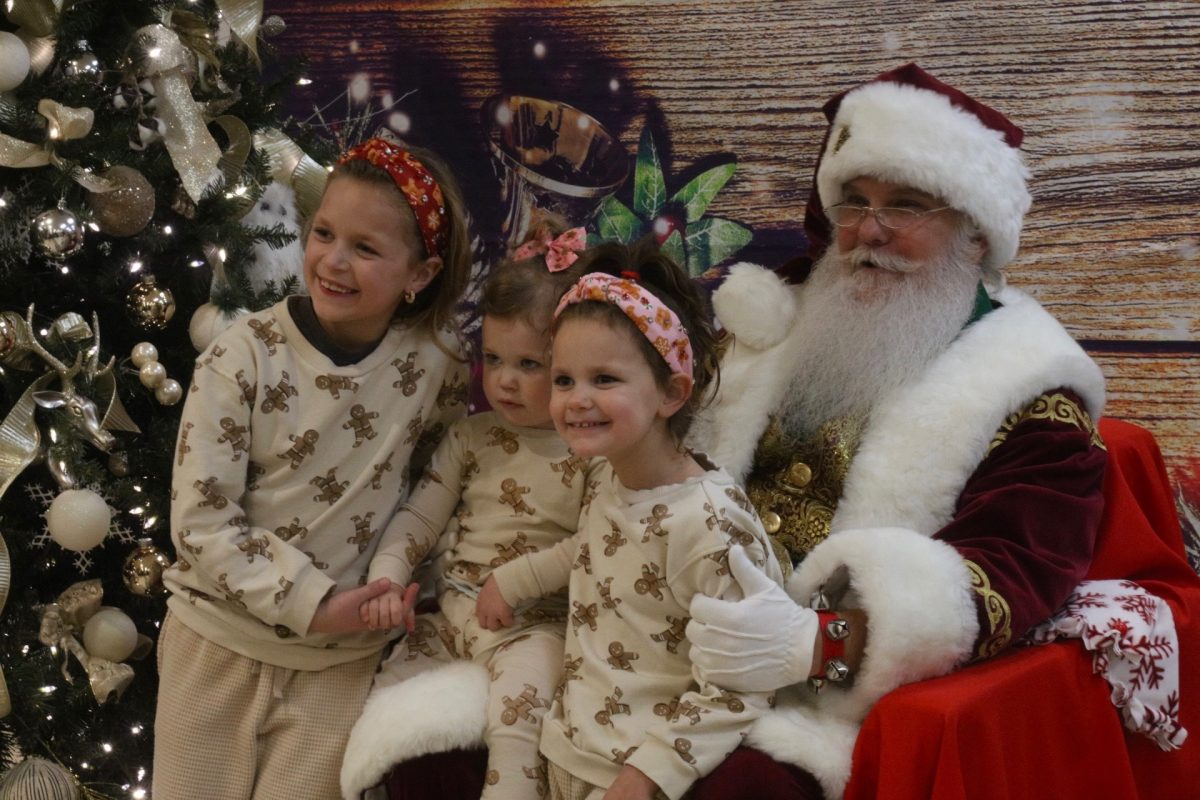 Three siblings, in matching pajamas, smile for a photo with Santa.