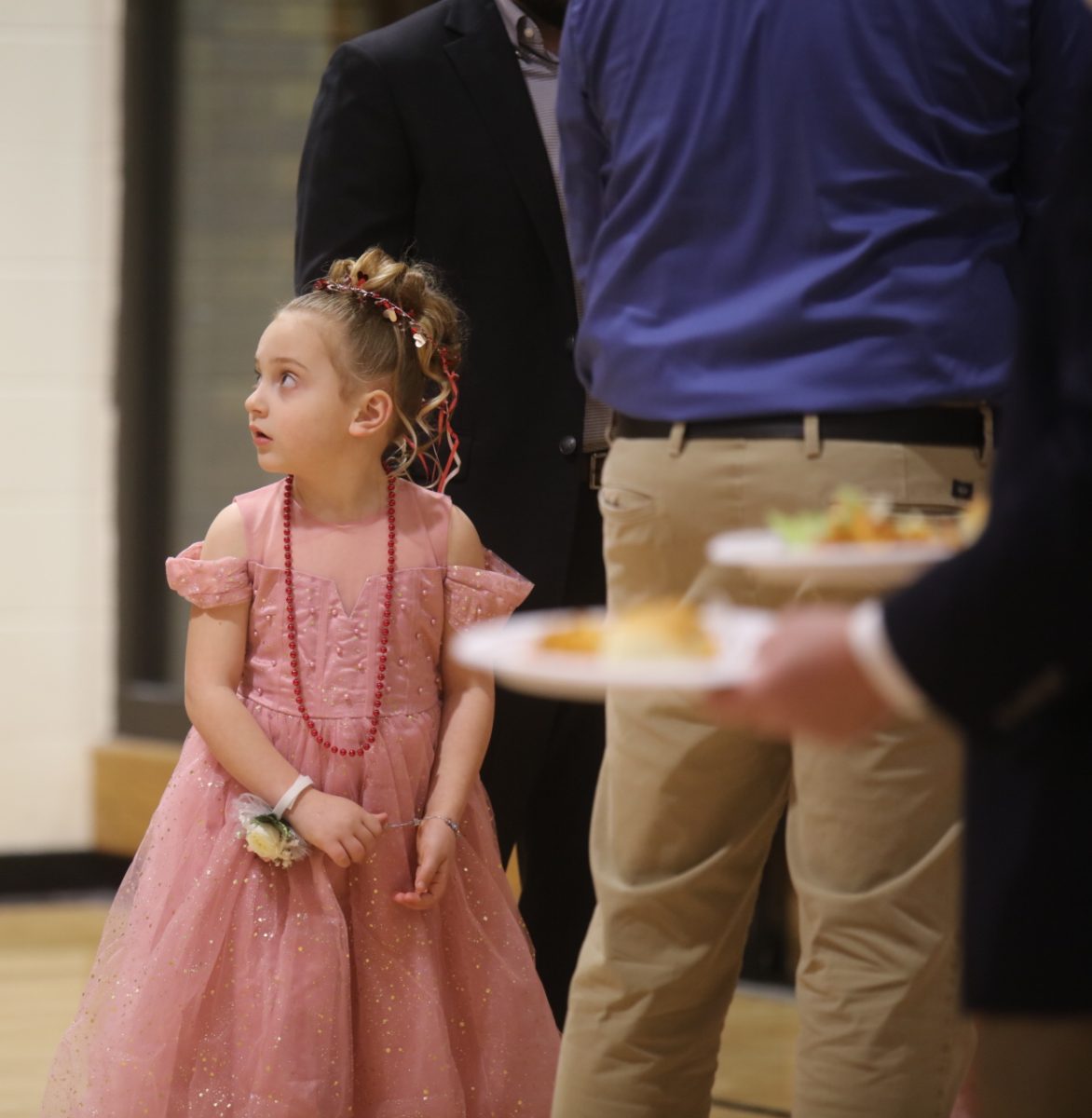 A little girl wearing a dress and beads waits in line for food at the Sweetheart Dance on Feb. 7.