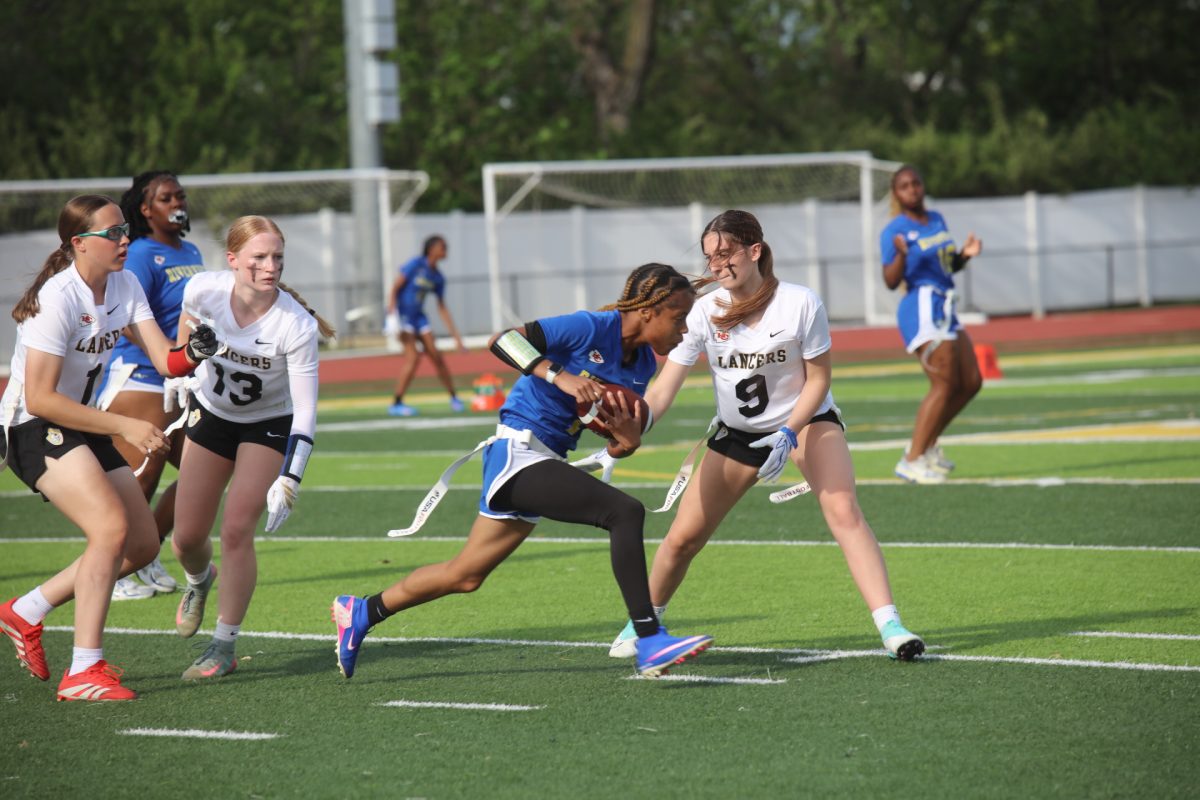Luthern South's Alyssa Thompson (#9) reaches for the flag of a Riverview Gardens player while Kate Riethmeier (#11) and Alison Stengel (#13) watch, waiting to react to the play.