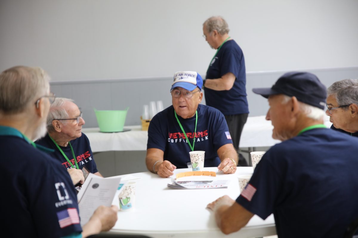 July 28 coffee talk attendees pictured deep in conversation. Once a month, a hot breakfast is served at the morning meeting in addition to the weekly coffee and donuts. Pictured behind those talking, a veteran serves himself breakfast.