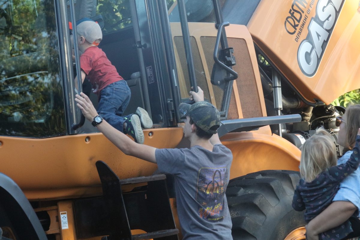 A young Touch-A-Truck attendee climbs into a large vehicle with the assistance of an onlooker.