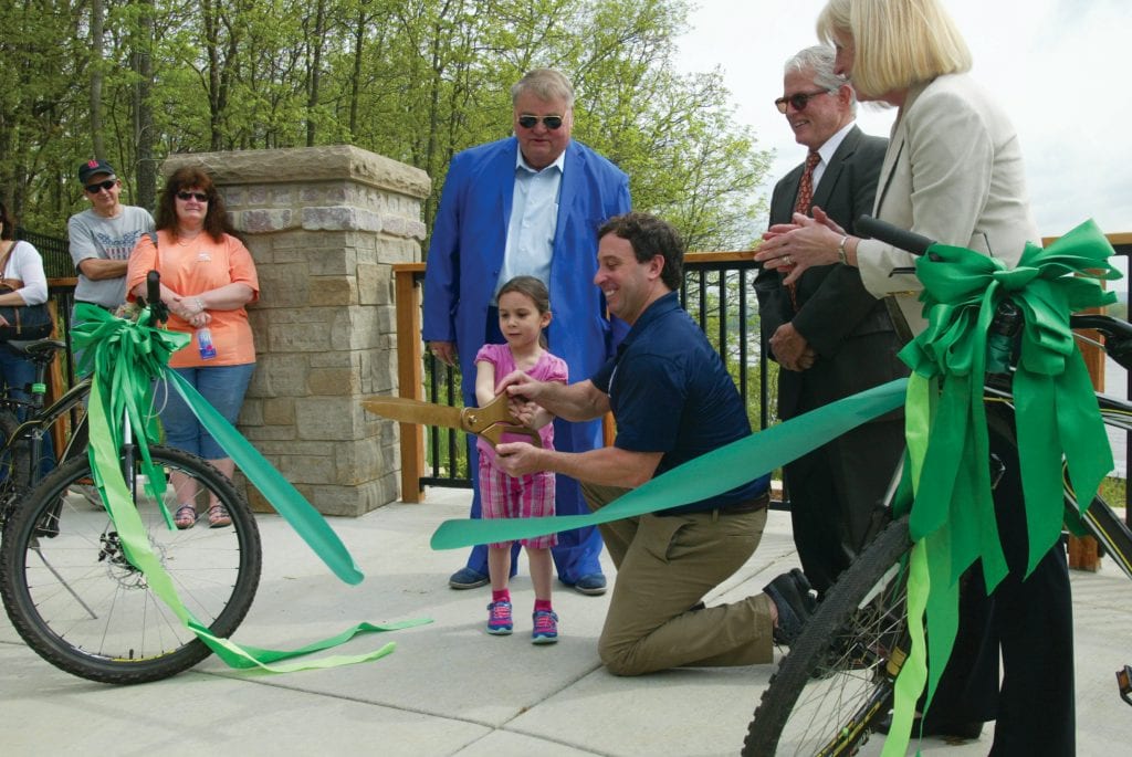 Stenger, kneeling, cuts the ribbon on the new Cliff Cave Park trail expansion in Oakville in May 2018, alongside county Parks Director Gary Bess, 5th District Councilman Pat Dolan, D-Richmond Heights, and Great Rivers Greenway Executive Director Susan Trautman. Stenger fought to get the trail built over the objections of 6th District Councilman Ernie Trakas, R-Oakville. Photo by Bill Milligan.