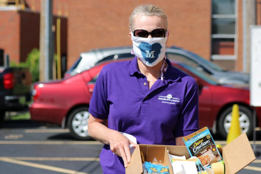 A Mehlville School District employee hands out emergency food boxes from Operation Food Search to students receiving grab-and-go meals while students are out of school during the pandemic. 