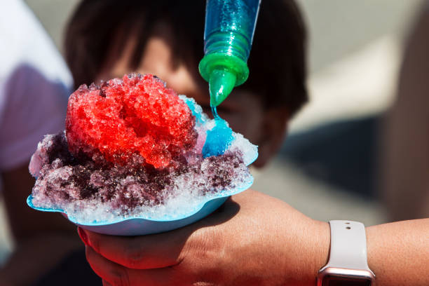 Closeup of woman's hand holding snow cone as she pours blue syrup onto the crushed ice.