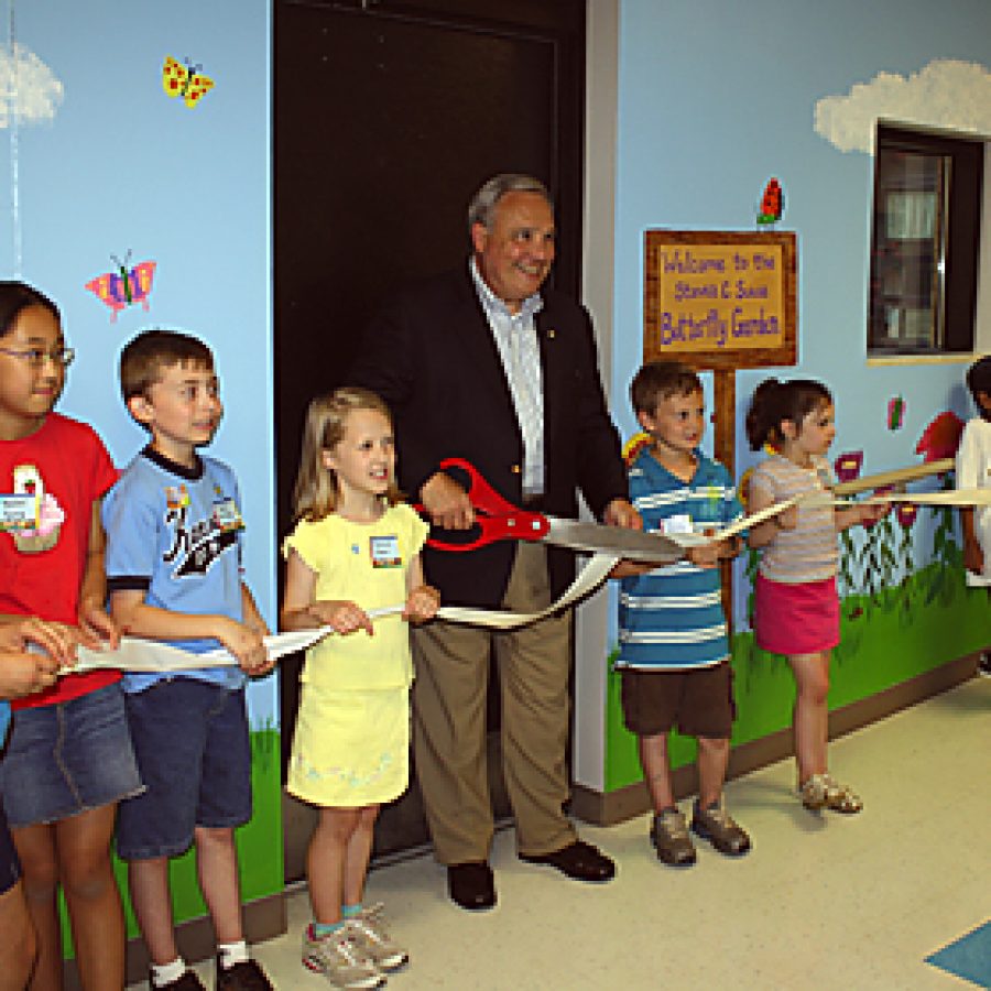 Former Kennerly Elementary School Principal Steven C. Suess cuts a ribbon celebrating a new butterfly garden that has been dedicated in his honor. The mural behind him was painted by art teacher Ann Clifton and features butterfly drawings made by pupils.