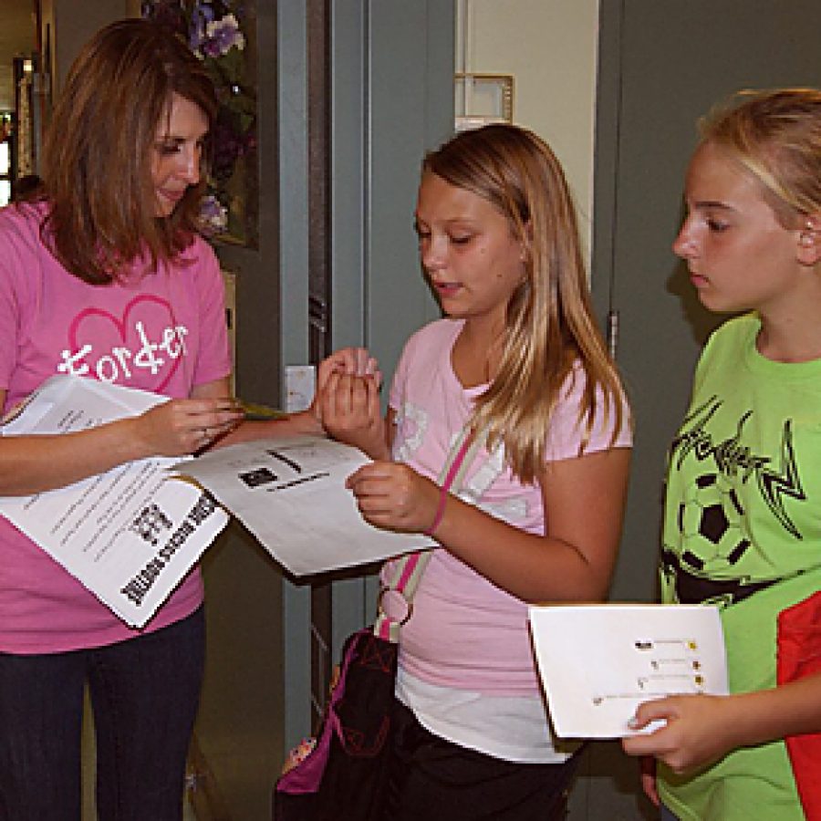 Forder Elementary fifth-graders Mackenzie Voiro, center, and Victoria Siebum, right, have their passports stamped by Special School District resource teacher Jenny Kirchhofer during the schools Passport Day.
